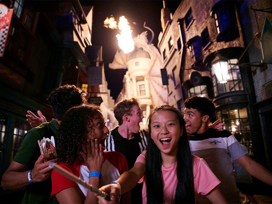 A group of friends laughs and poses in front of the fire-breathing dragon in Diagon Alley