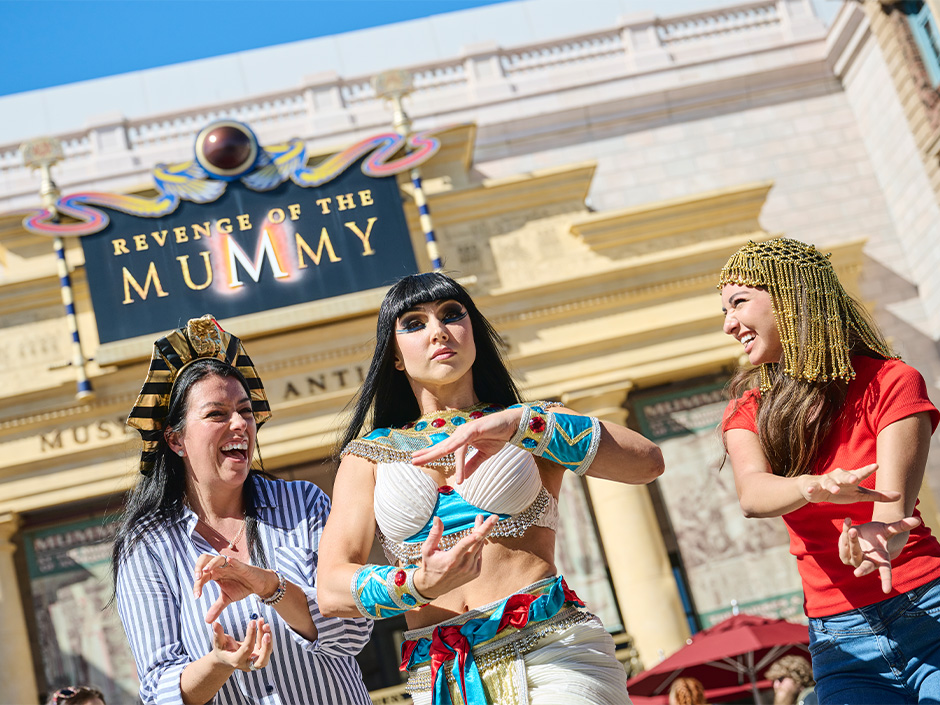 Two girls smile and pose with a character performer outside of Revenge of the Mummy