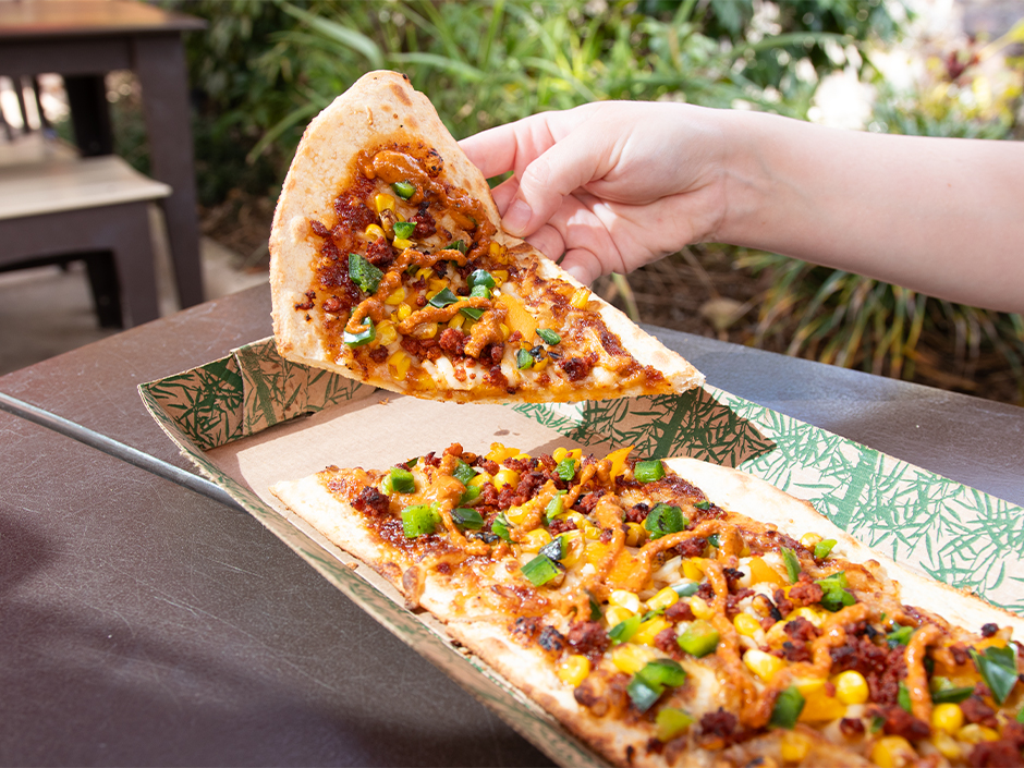 A guest picks up a slice of a Vegan Longboard Pizza from Kohola Reef Restaurant at Volcano Bay
