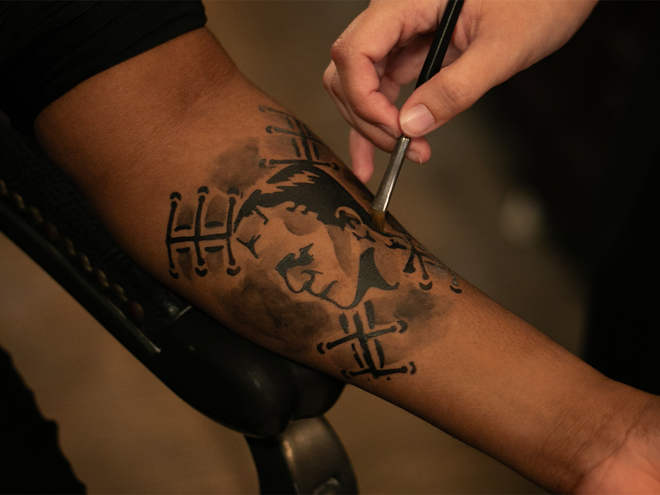 A makeup artist at the Darkmoor Monster Makeup Experience paints a temporary tattoo of Frankenstein on a guest's arm
