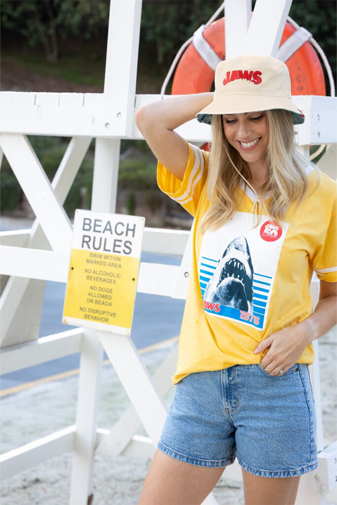 Uma garota sorri e posa com uma camiseta do aniversário de Jaws e um chapéu de balde