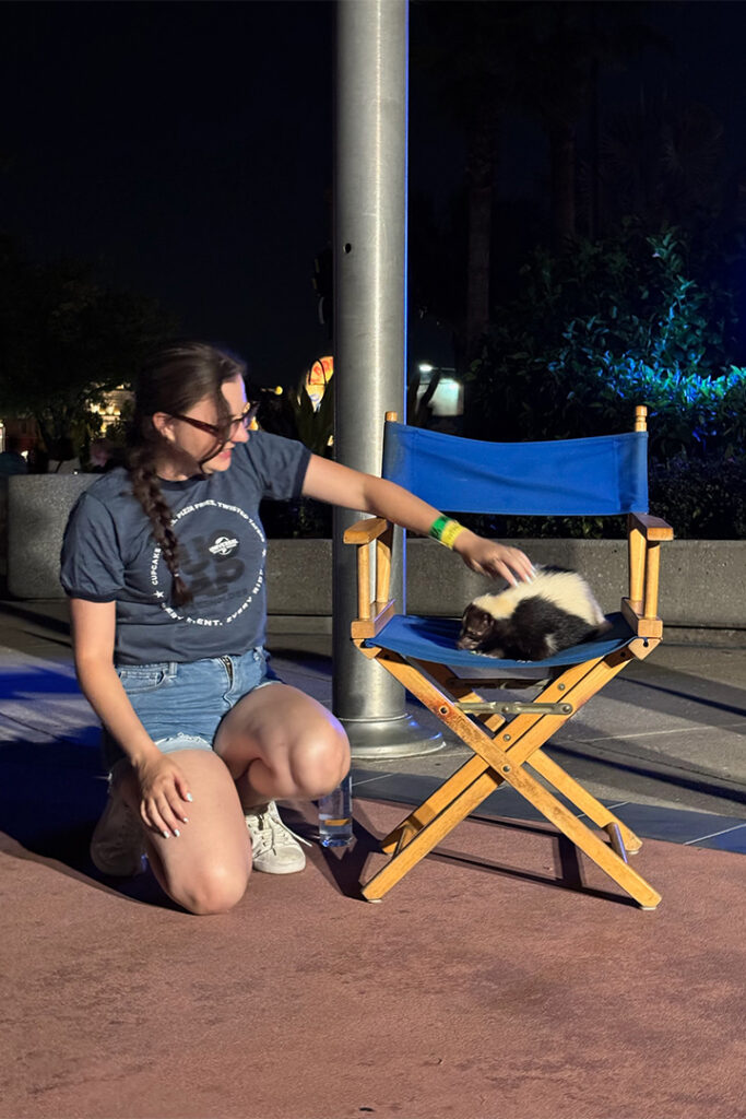 A guest smiles and poses with Dusty the Skunk from Animal Actors on Location