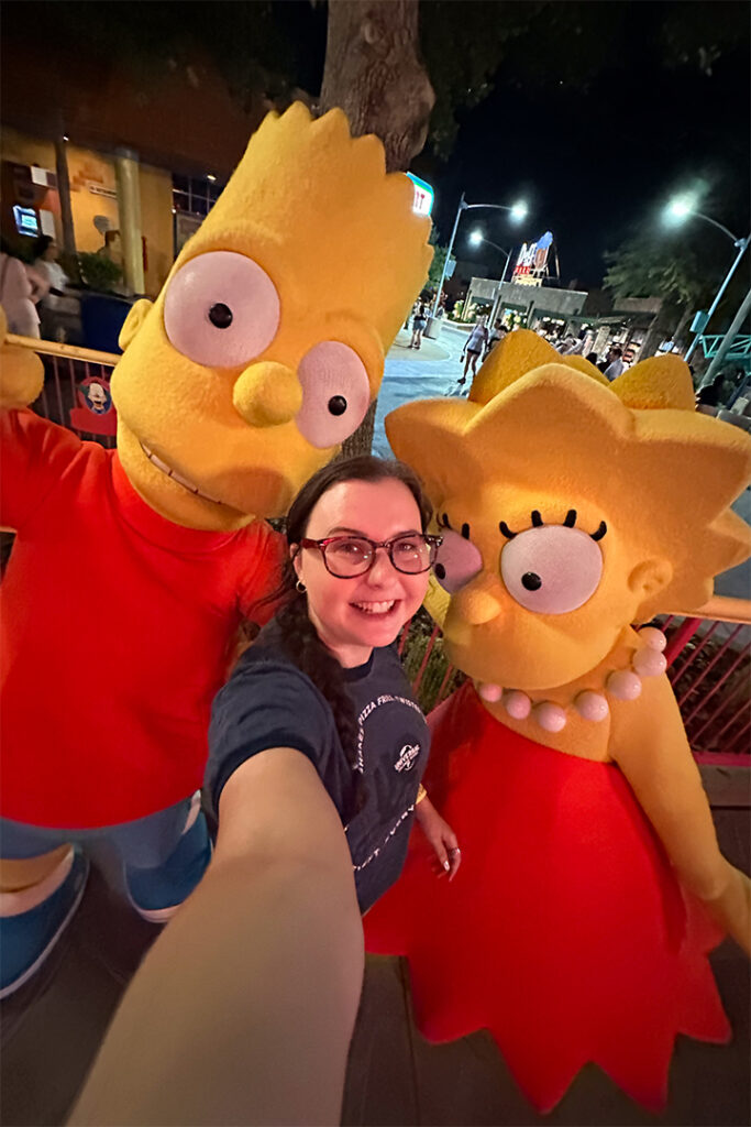 A guest smiles and poses with Bart and Lisa Simpsons