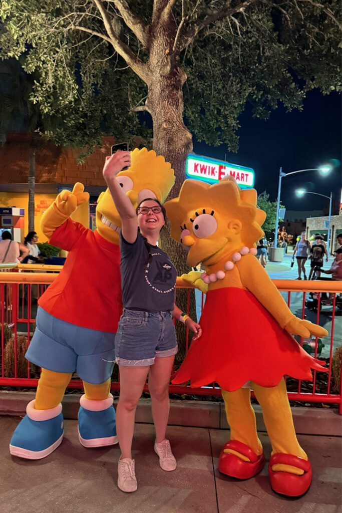 A guest smiles and poses with Bart and Lisa Simpsons