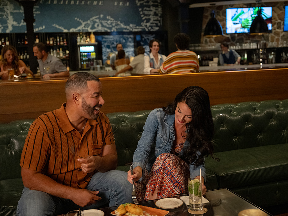 A couple laughs and enjoys a drink in Strongwater Tavern at Loews Royal Pacific Resort