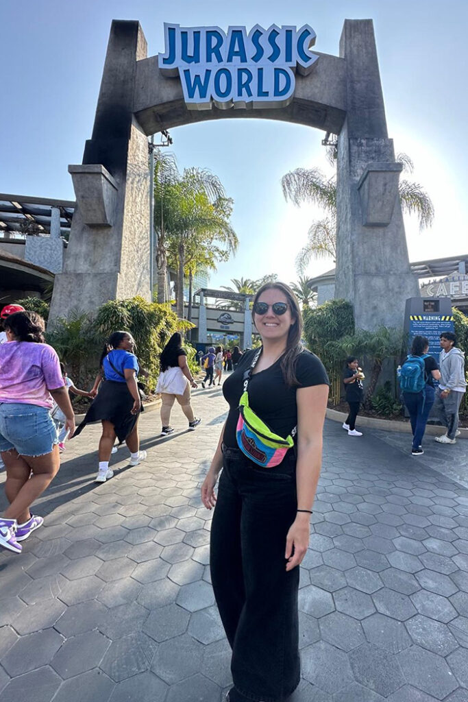 Writer Julia Goncalves poses in front of Jurassic World at Universal Studios Hollywood.