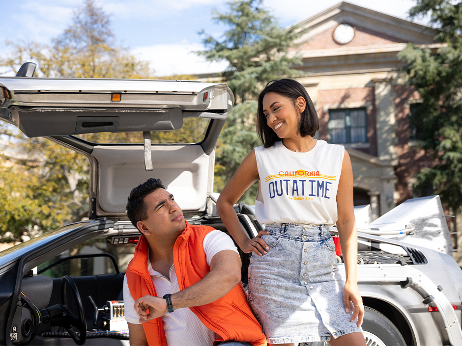 Two guests in Back to the Future merchandise pose with a time machine on the Universal Studios Hollywood Backlot