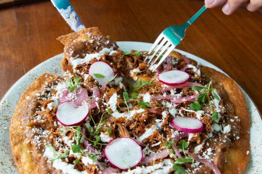 A fork and knife cut into Tlayuda from Antojitos Authentic Mexican Food in Universal CityWalk