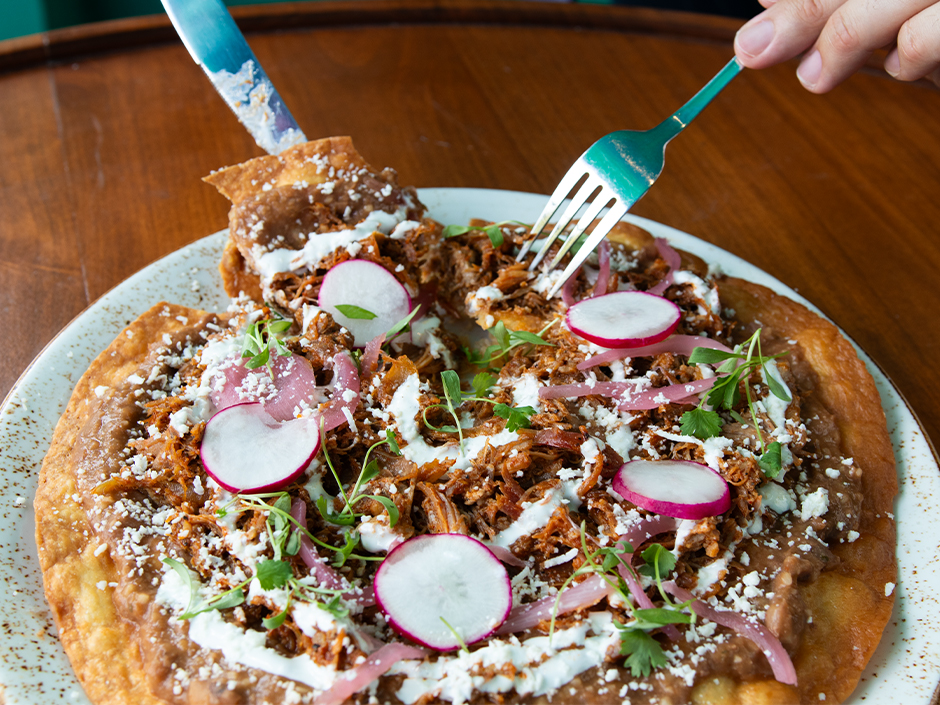 A fork and knife cut into Tlayuda from Antojitos Authentic Mexican Food in Universal CityWalk