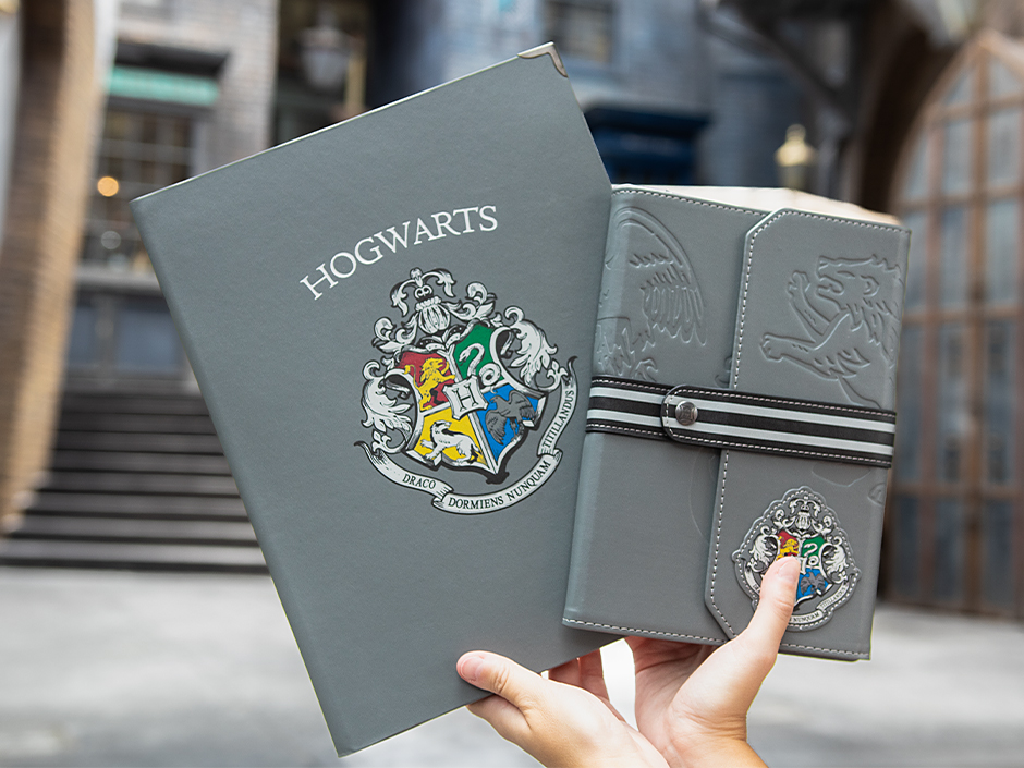 Hands holding two gray Back to Hogwarts crest themed notebooks at Universal Orlando Resort.