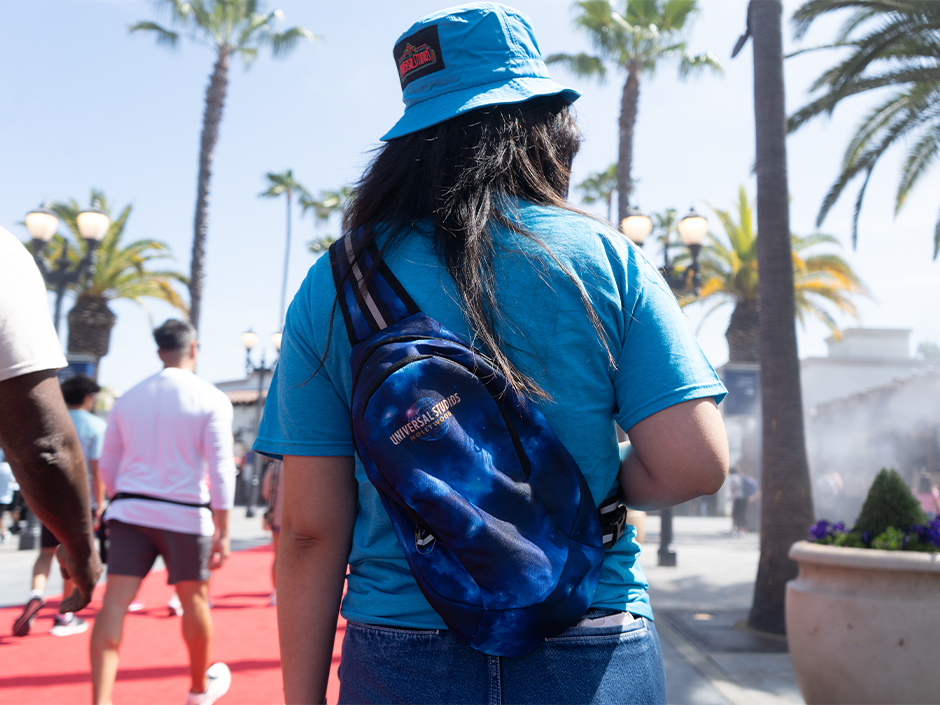 The back of a person in a Universal hat and wearing a Universal backpack in front of Universal Studios Hollywood