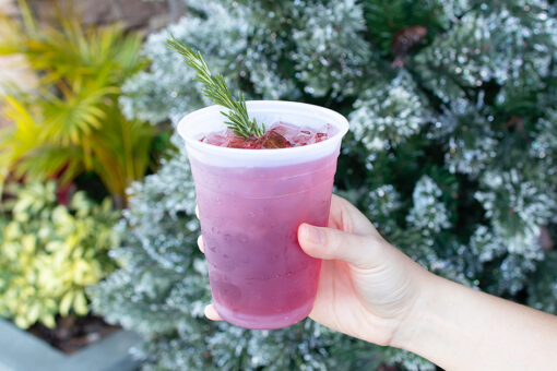A hand holding the Gin-gile Bells mocktail in front of a Christmas Tree