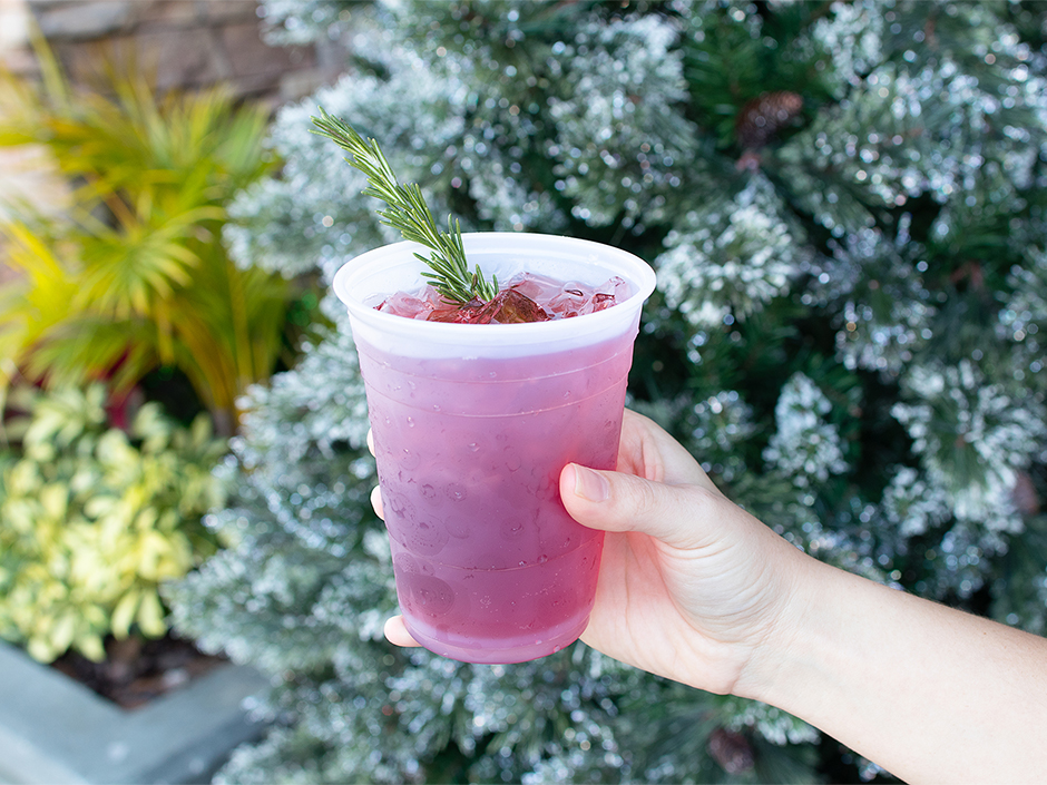 A hand holding the Gin-gile Bells mocktail in front of a Christmas Tree