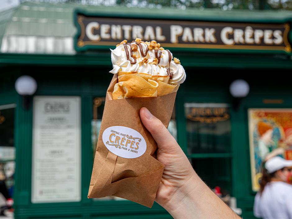 A hand holds up a crepe in front of Central Park Crepes in Universal Studios Florida