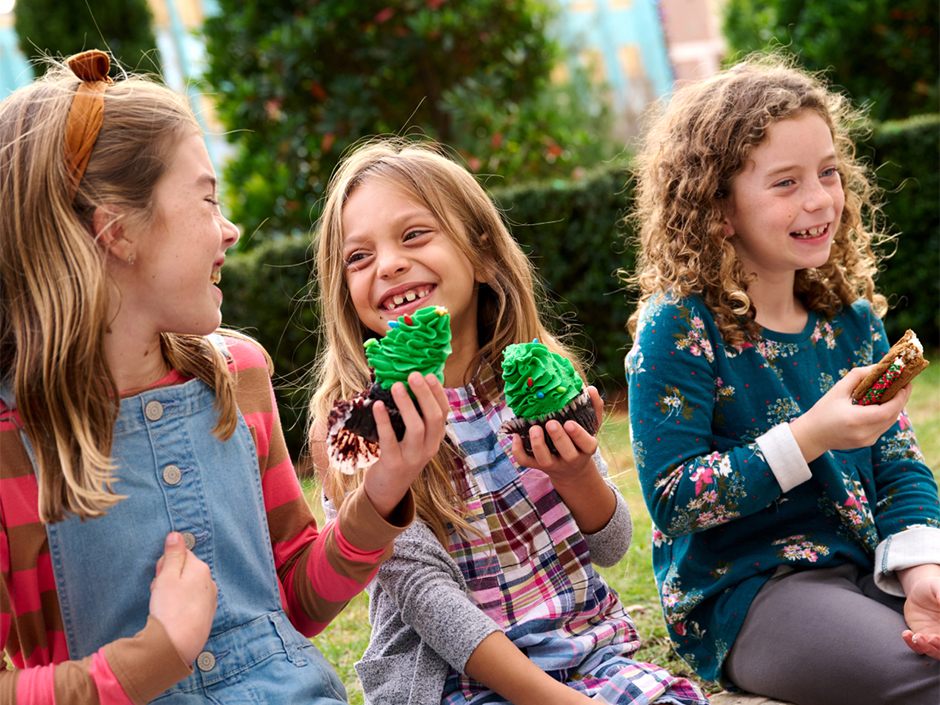 A trio of girls smiles and eats cupcakes together while sitting on a curb at Universal Studios Florida