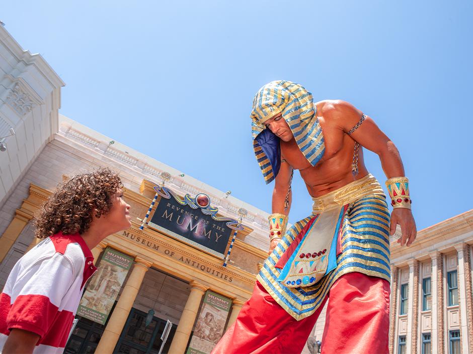 A tomb guard leans over toward a guest in front of Revenge of the Mummy