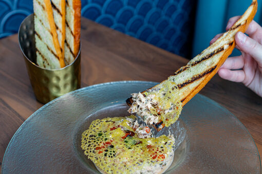 Hand dipping toasted bread into the holiday Smoked Salmon Rillette at Atlantic in Universal Epic Universe.