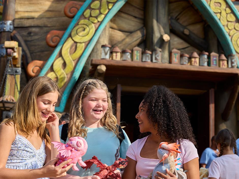 Three girls smile with dragon toys outside of How to Treat Your Dragon in How to Train Your Dragon - Isle of Berk