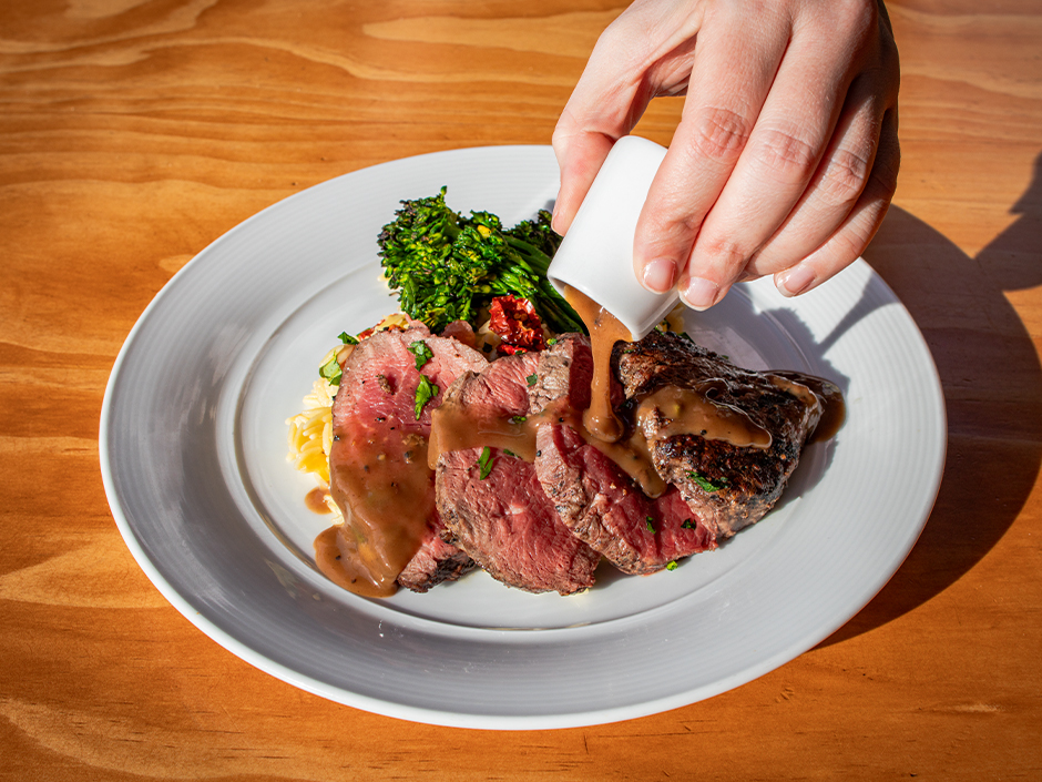 Hand pouring chianti wine reduction over Broiled Chateaubriand at VIVO Italian Kitchen for Valentine's Day.