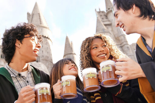 A group of guests enjoying mugs of Butterbeer in front of Hogwarts castle.