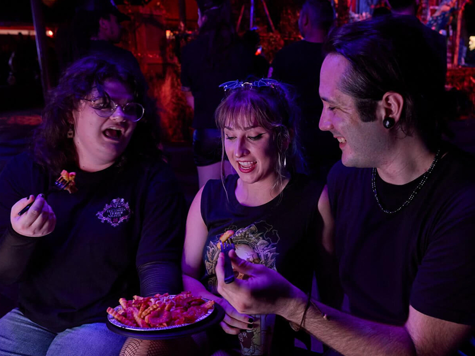Friends chat while eating pizza fries at Halloween Horror Nights. 