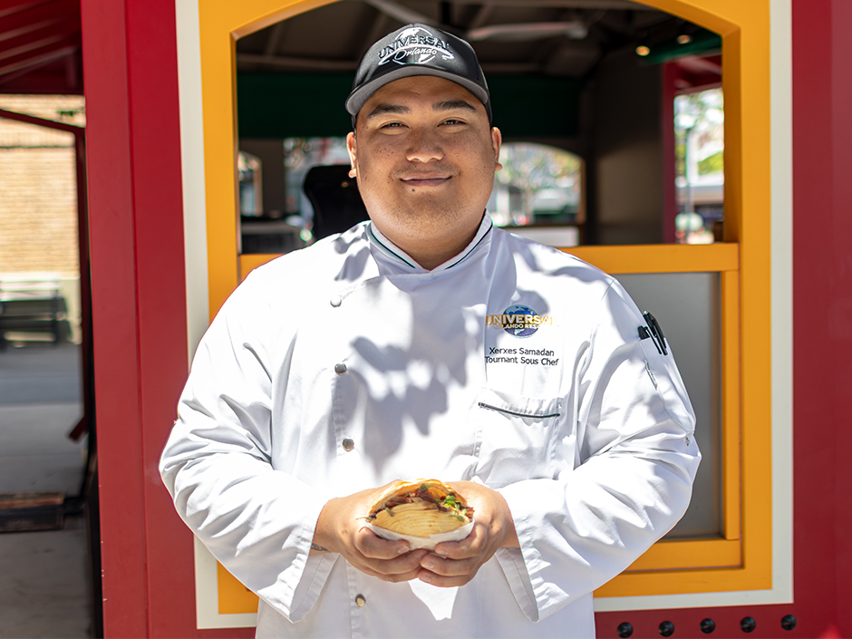 Chef Xerxes holding a Roujiamo in front of the San Fran Street Cart in Universal Studios Florida for AANHPI Heritage Month.