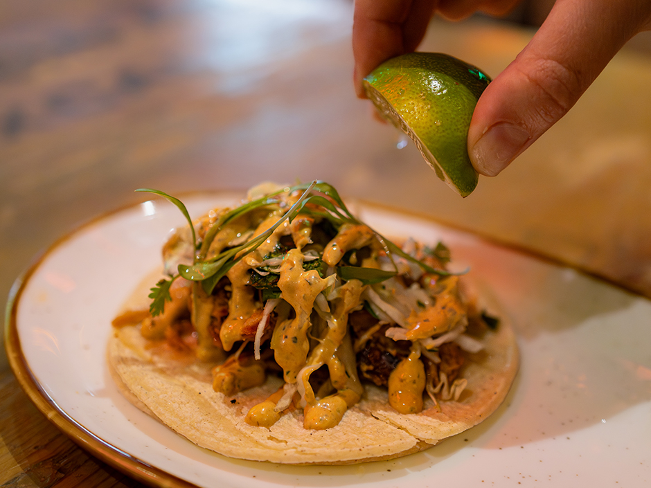 A hand squeezing a lime wedge over a chicken tinga taco at Antojitos Authentic Mexican food in Universal CityWalk for Cinco de Mayo.