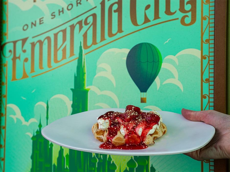 A hand holding up the Strawberry Cheesecake Waffle at Emerald City Eats