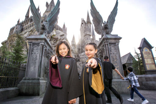 Two children posing with wands in front of Hogwarts Castle