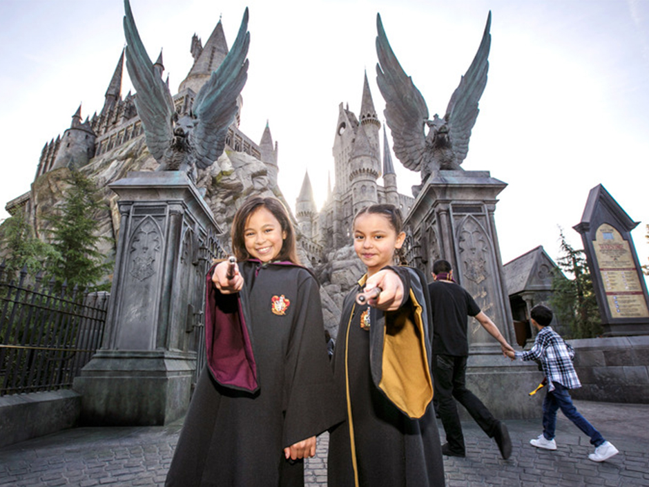 Two children posing with wands in front of Hogwarts Castle