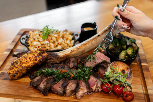 Hand holding a fork with a piece of Tomahawk Ribeye