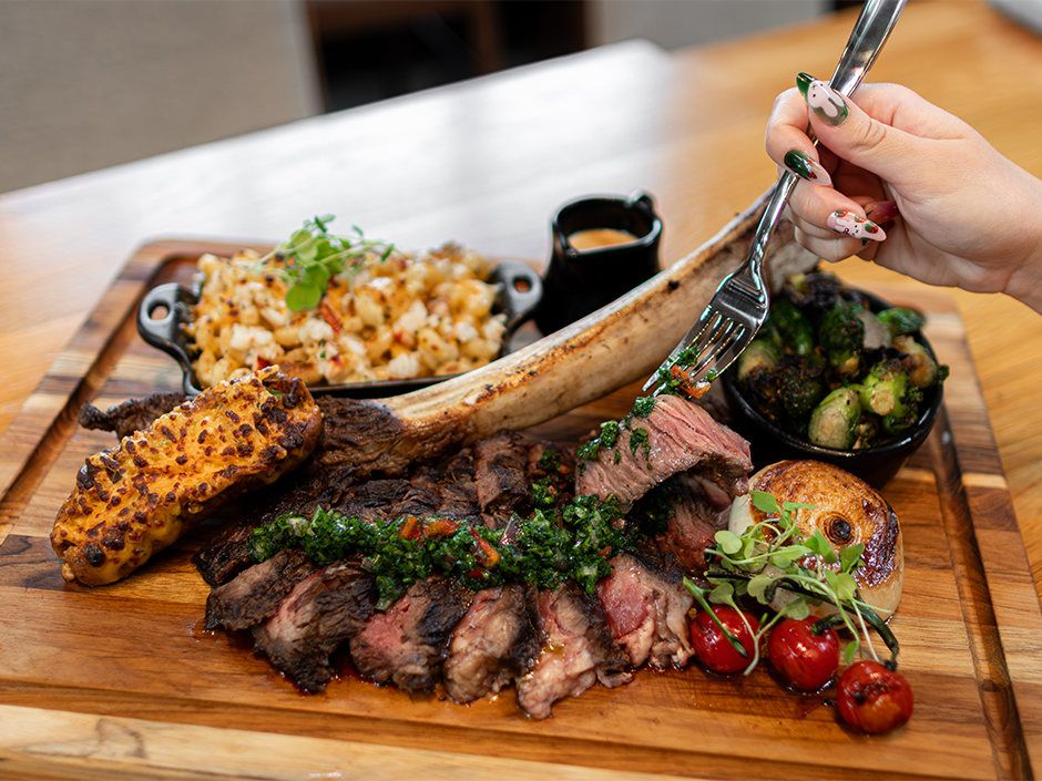 Hand holding a fork with a piece of Tomahawk Ribeye