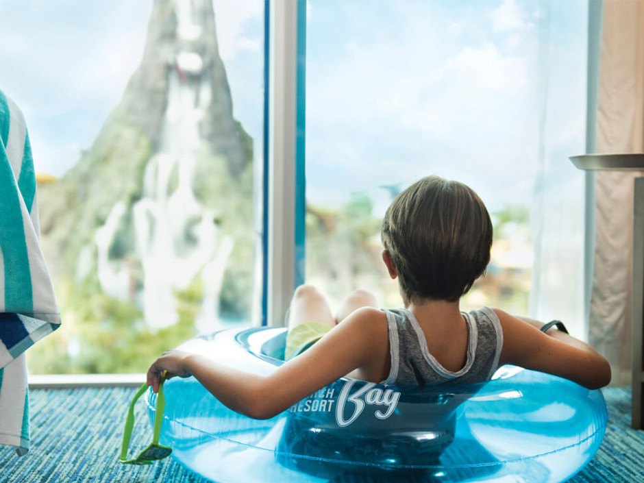 A child laying in a floatie in a Cabana Bay room looking at the Volcano at Volcano Bay.