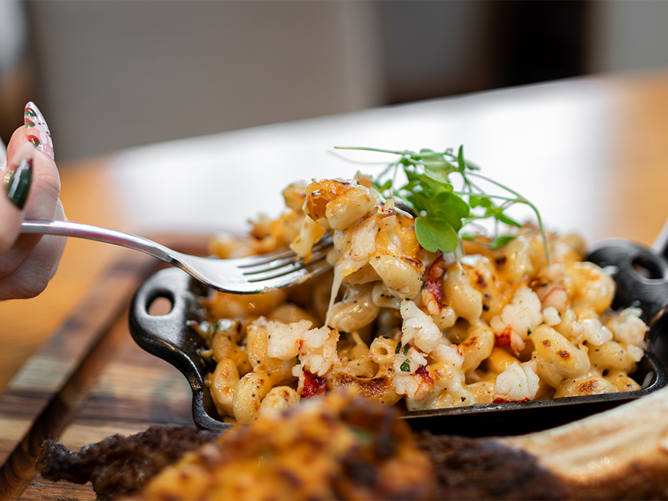 Hand dipping fork into Black Truffle Lobster Mac and Cheese at Bigfire for Father's Day.
