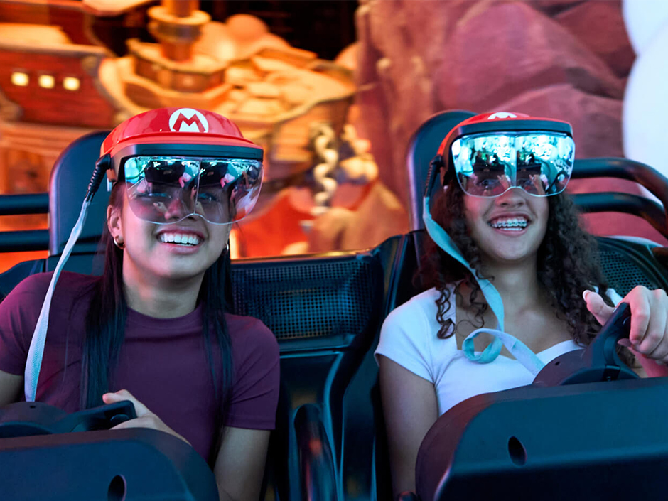 Teens smile as they ride Mario Kart: Bowser's Challenge.