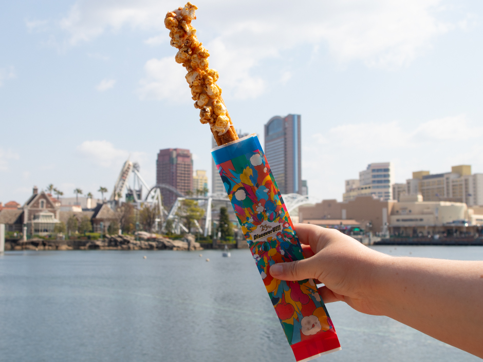 A churro covered in popcorn with the skyline of Universal Studios Japan in the background