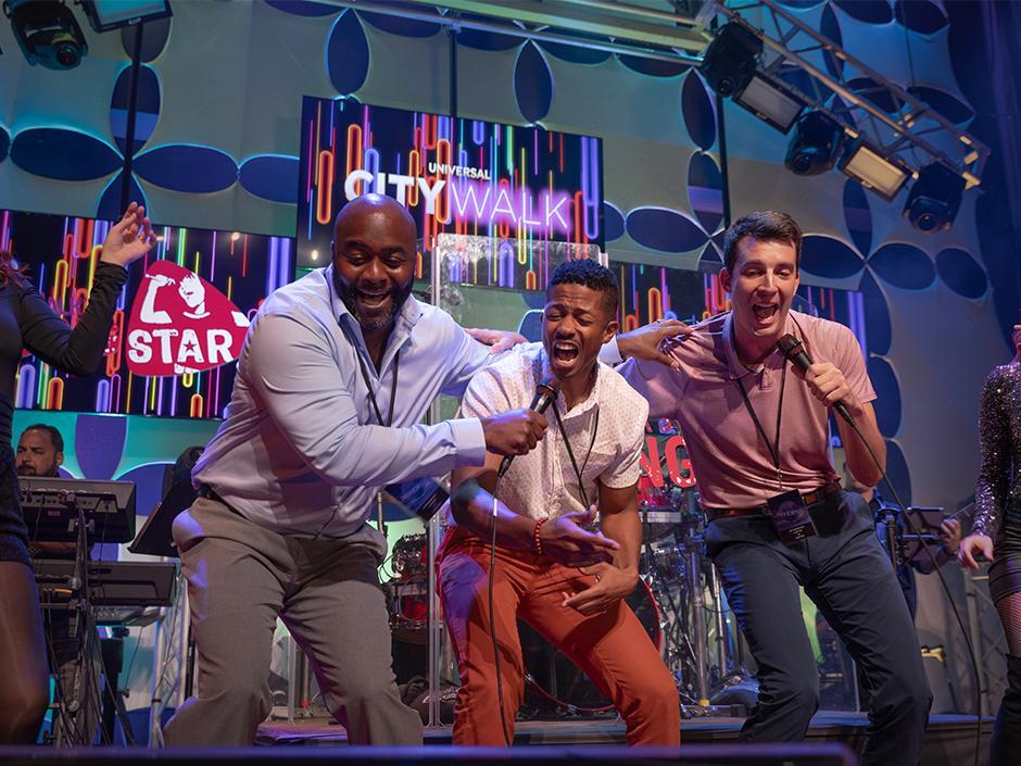 Three guests laugh and sing karaoke together onstage at Rising Star in Universal CityWalk