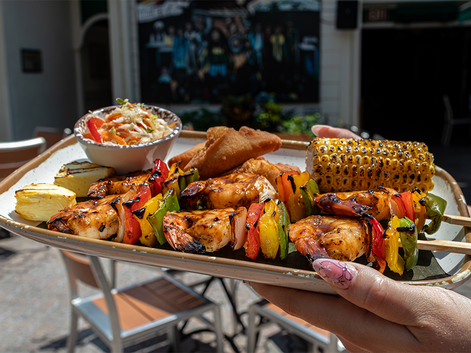 Hands holding a plate of shrimp skewers at Bob Marley's in Universal CityWalk for Jamaica's Independence Day.