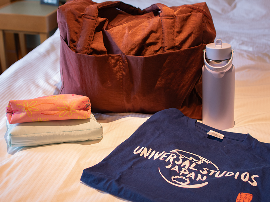 A bag and a handful of items (shirt, water bottle, smaller bags) sitting on a bed.