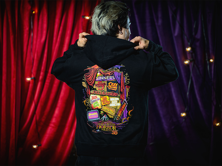 A guest poses and shows off the back of their 2026 HHN logo hoodie