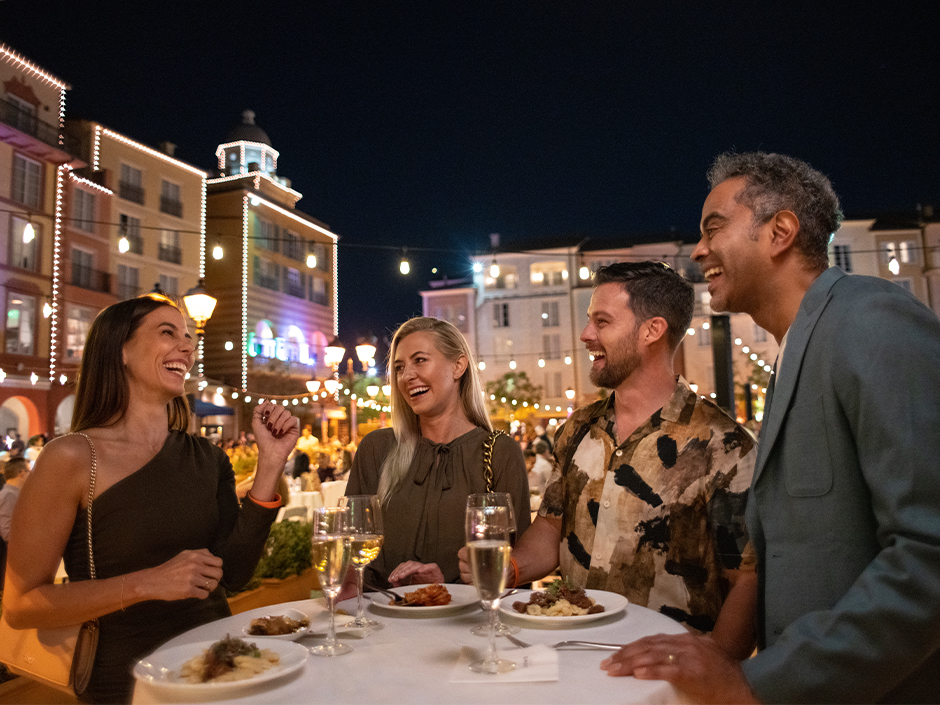 A group of friends smiling at each other as they sip on wine and enjoy bites at a Harbor Nights event