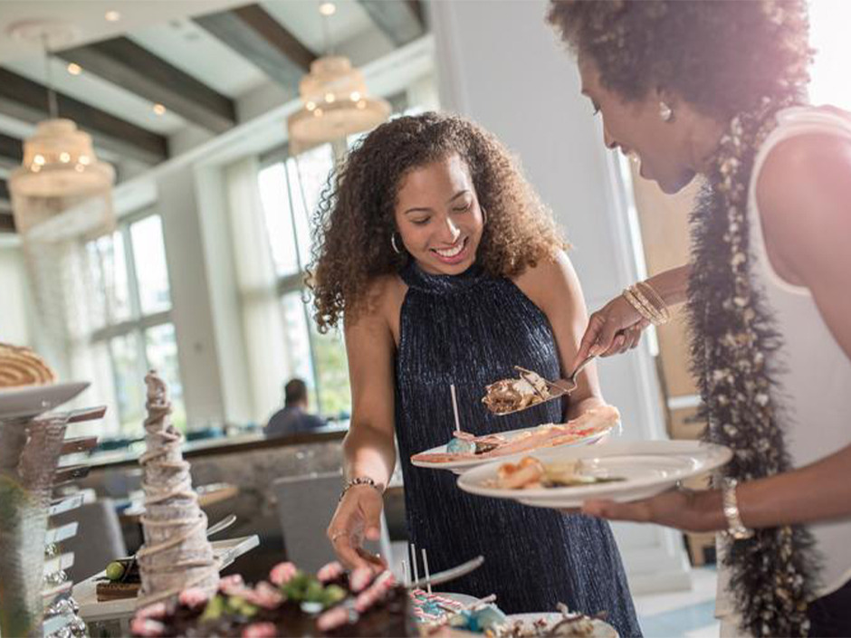 Two friends smiles as they fill their plates with holiday treats at Loews Sapphire Falls Resort