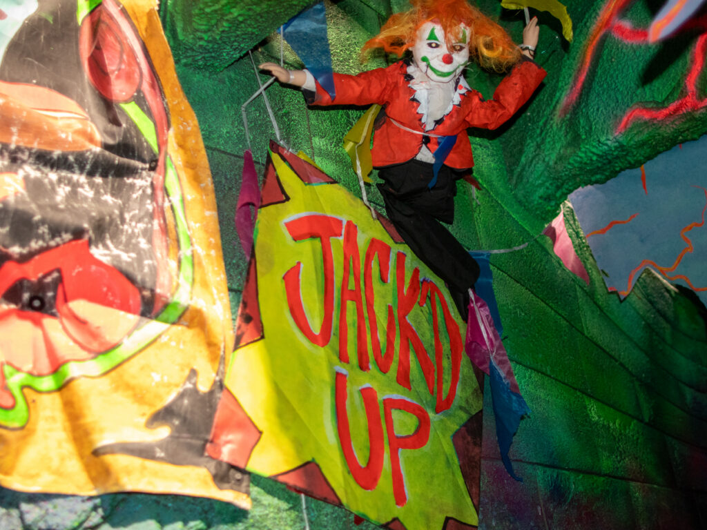 A wall in the Jack & Oddfellow: Chaos & Control house at Halloween Horror Nights 2026. A clown doll is next to a sign reading "Jack'D Up"