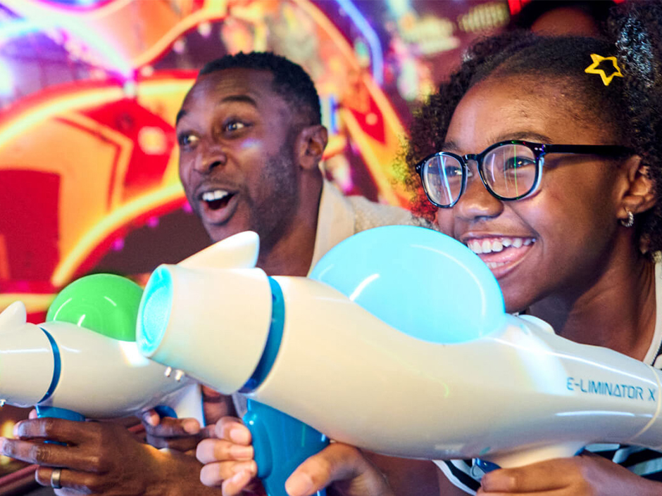 A father and daughter smile as they blast their way through Illumination's Villain-Con Minion Blast