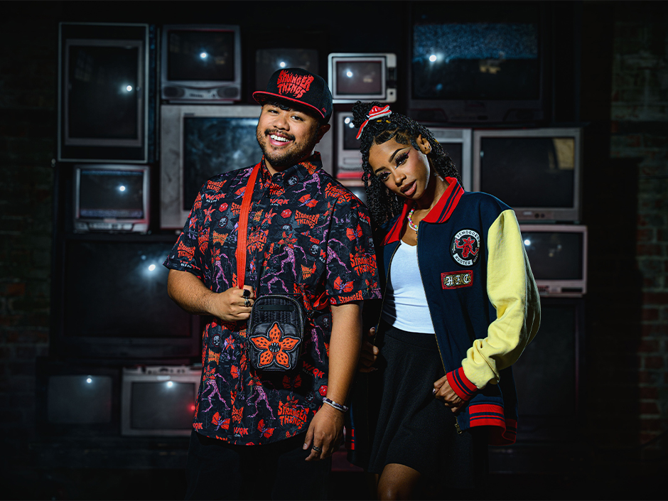 Two guests pose side by side with Stranger Things 5 merch, including a shirt, hat, and jacket
