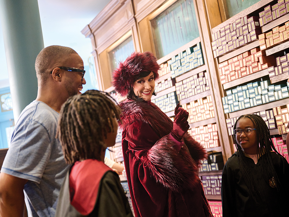 Cosme Acajor shows a wand to a family inside her shop at Epic Universe
