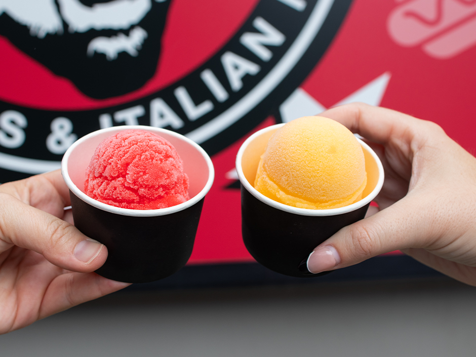 Two guests hold up cherry and mango Italian ice from Fat One's at Universal CityWalk