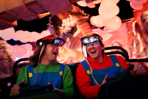 Two boys smile at each other and laugh while riding Mario Kart: Bowser's Challenge at Universal Epic Universe