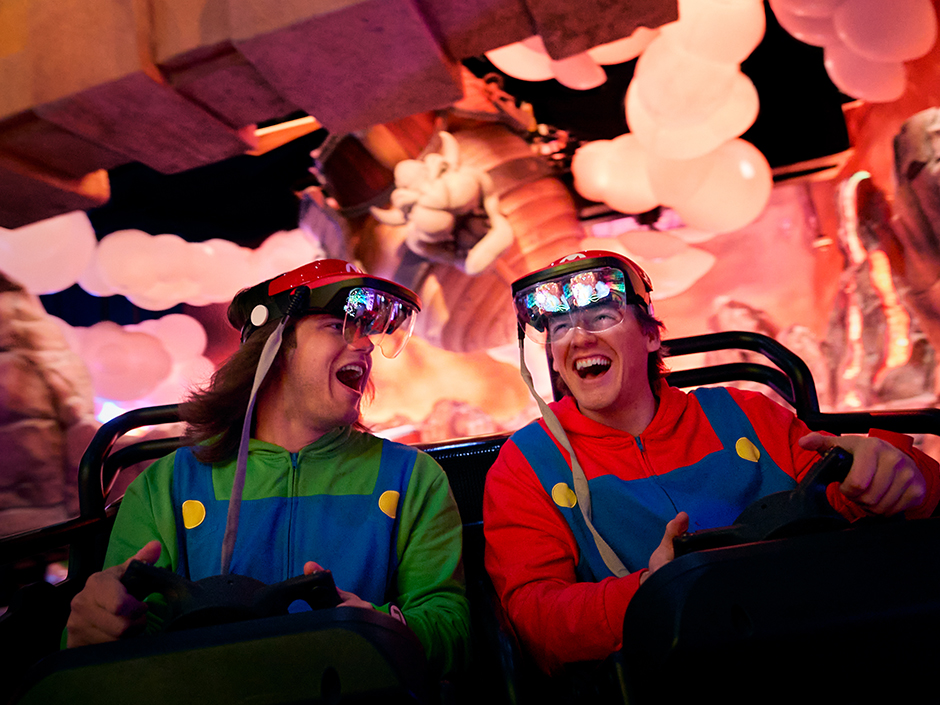 Two boys smile at each other and laugh while riding Mario Kart: Bowser's Challenge at Universal Epic Universe