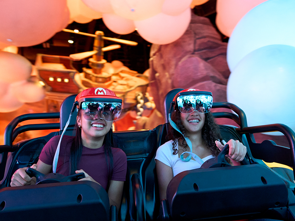 Two girls smile and steer their karts on Mario Kart: Bowser's Challenge in Epic Universe